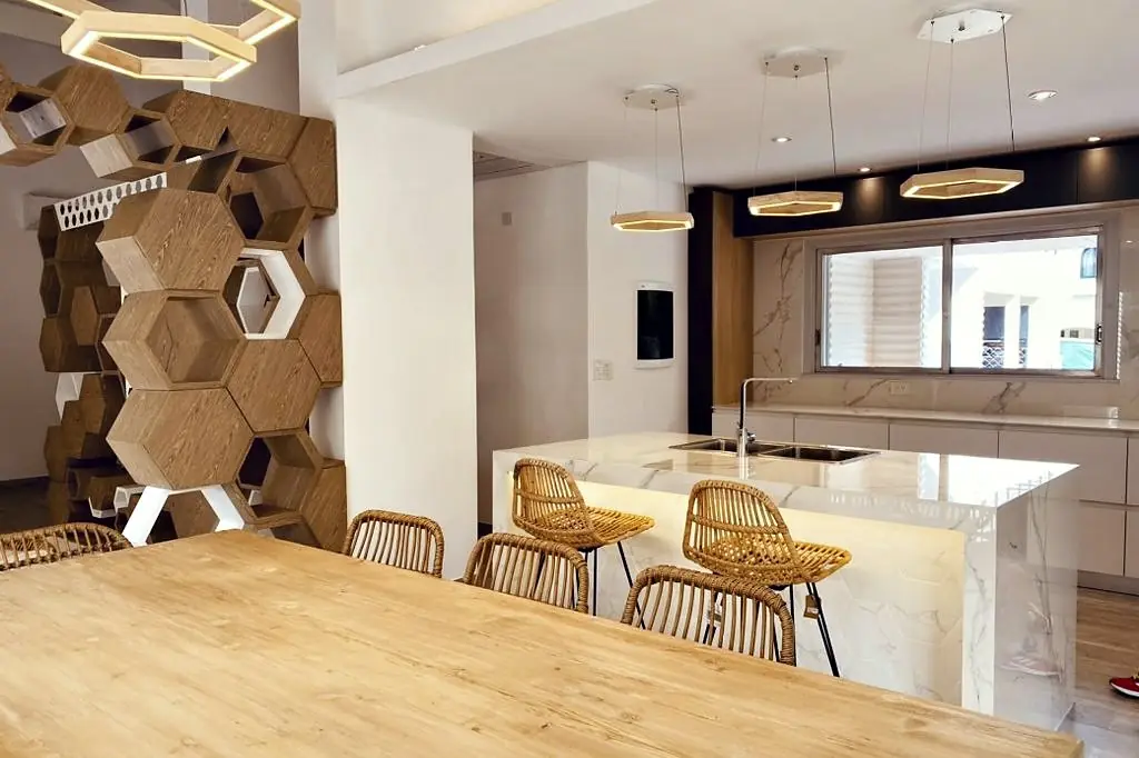 Cocina de la vivienda AVNZ: isla de mármol, lámparas hexagonales y mueble de hexágonos de madera