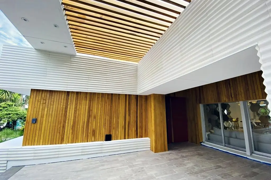 Acceso de la vivienda AVNZ: pérgola de madera, muro de listones y puerta roja