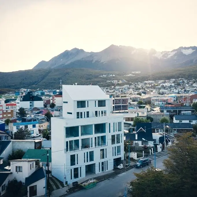 Edificio blanco de viviendas visto desde el aire, con Ushuaia y la cordillera detrás