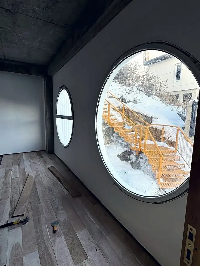 Interior de The Minimal: ventana circular hacia la escalera naranja nevada, piso de madera