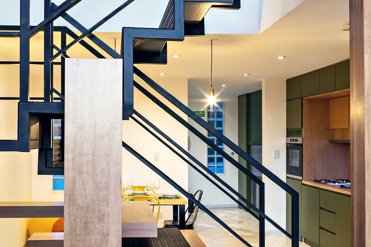 Escalera metálica negra, columnas de madera y cocina verde en un dúplex de Miradores del Susana