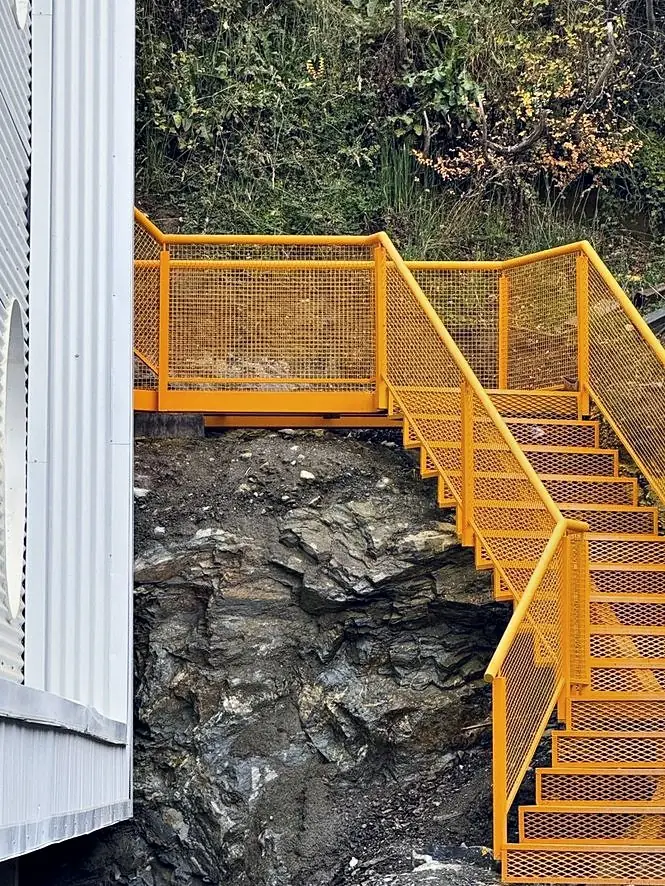 Escalera metálica naranja de The Minimal anclada en la roca