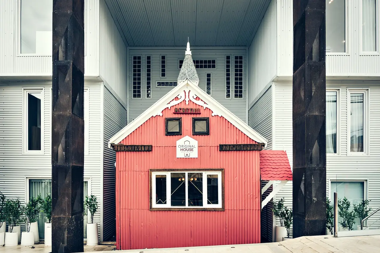 La casa roja de 1920 conservada entre los pórticos de corten, de día