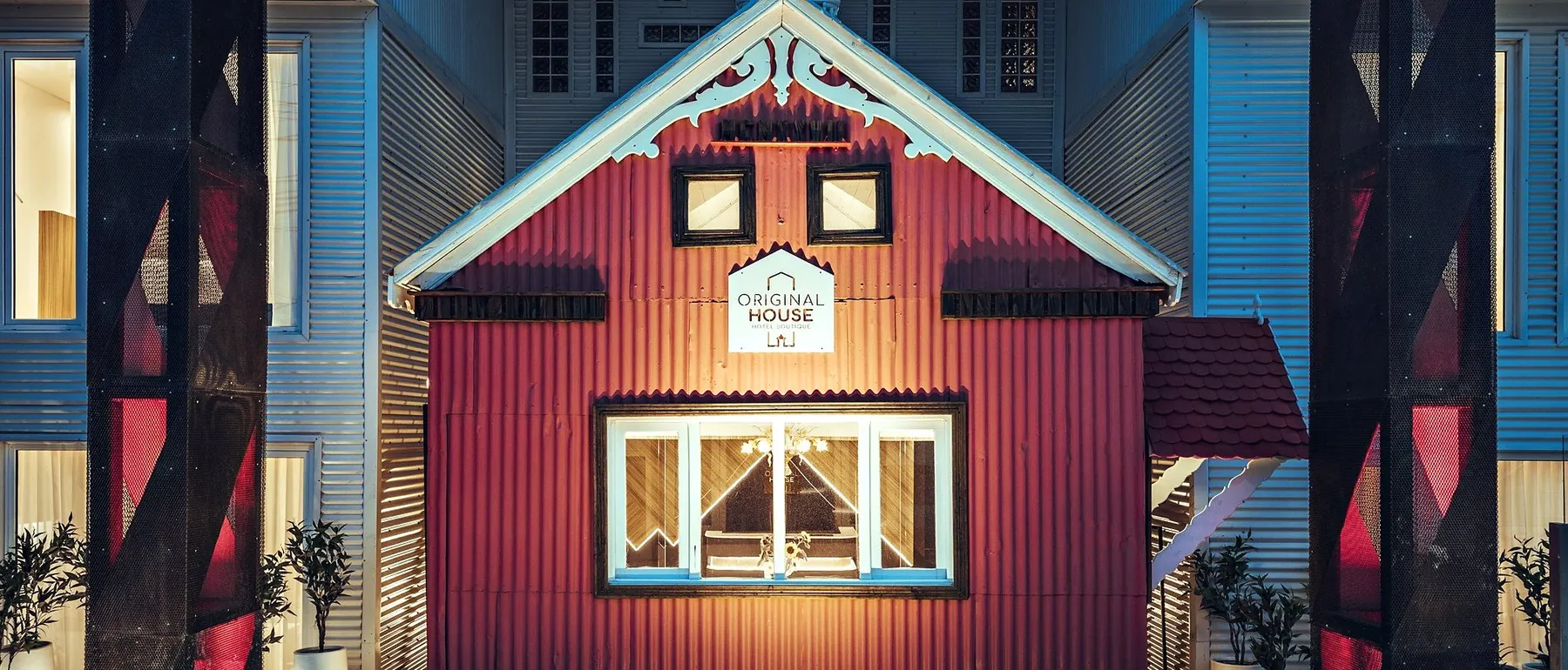 Original House de noche: la casa roja histórica bajo los pórticos de acero corten iluminados