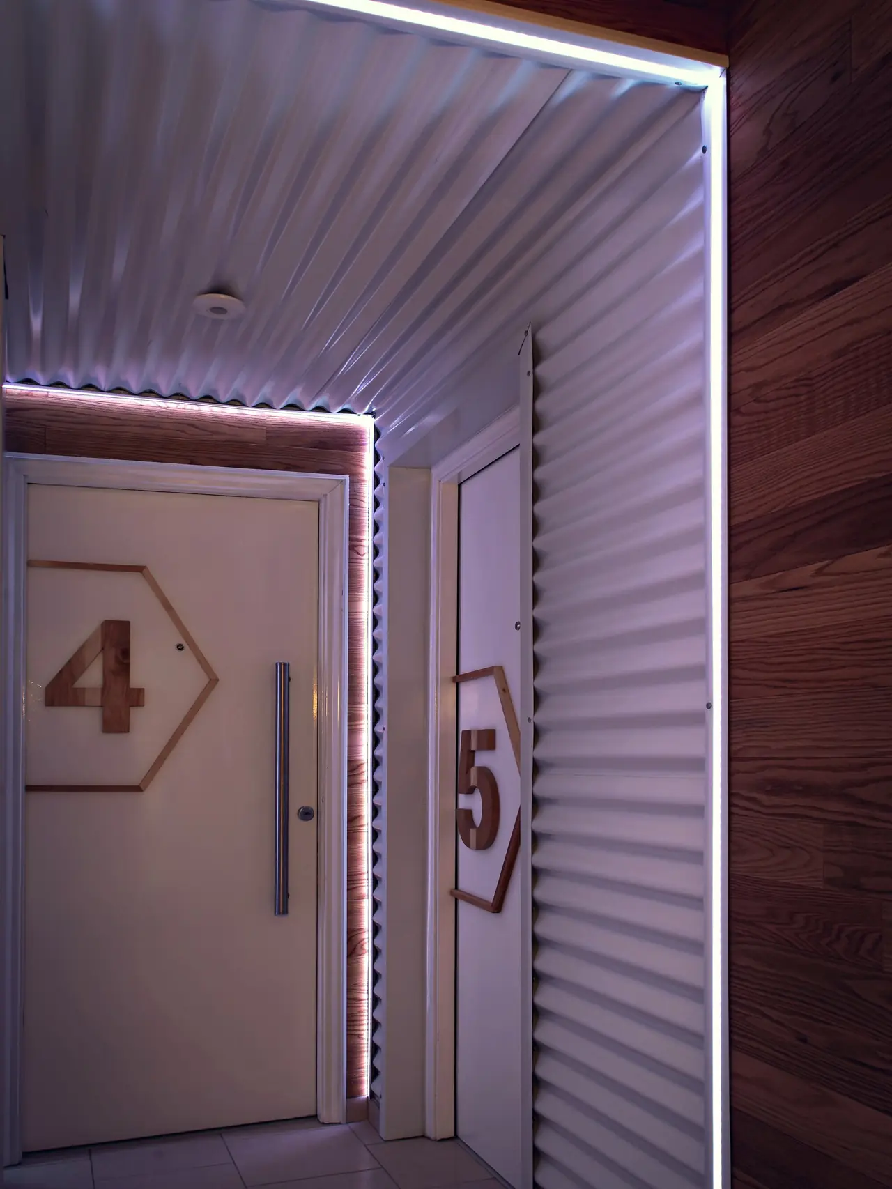 Pasillo de chapa blanca y madera con tiras de luz LED y puertas numeradas