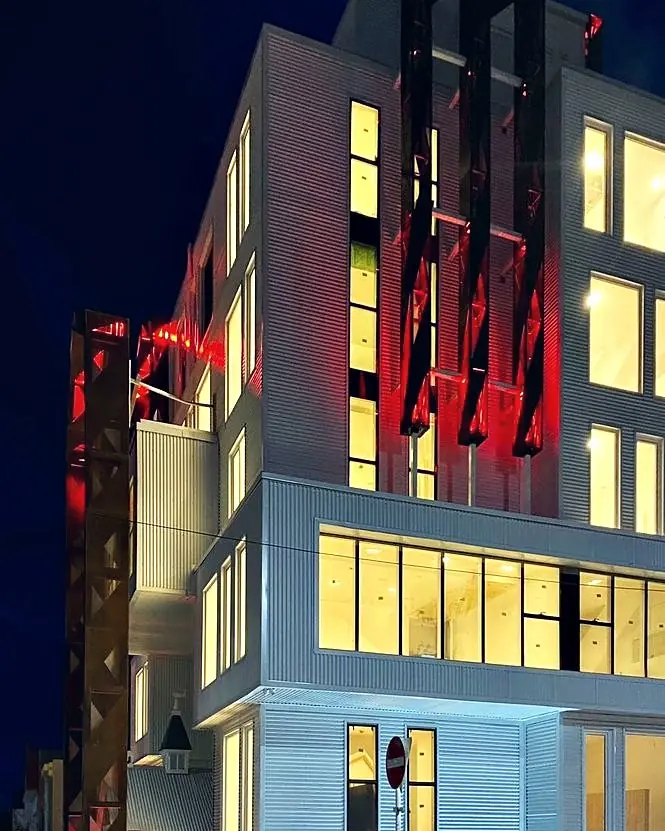 Edificio de chapa blanca de noche, con los pórticos de acero corten iluminados en rojo